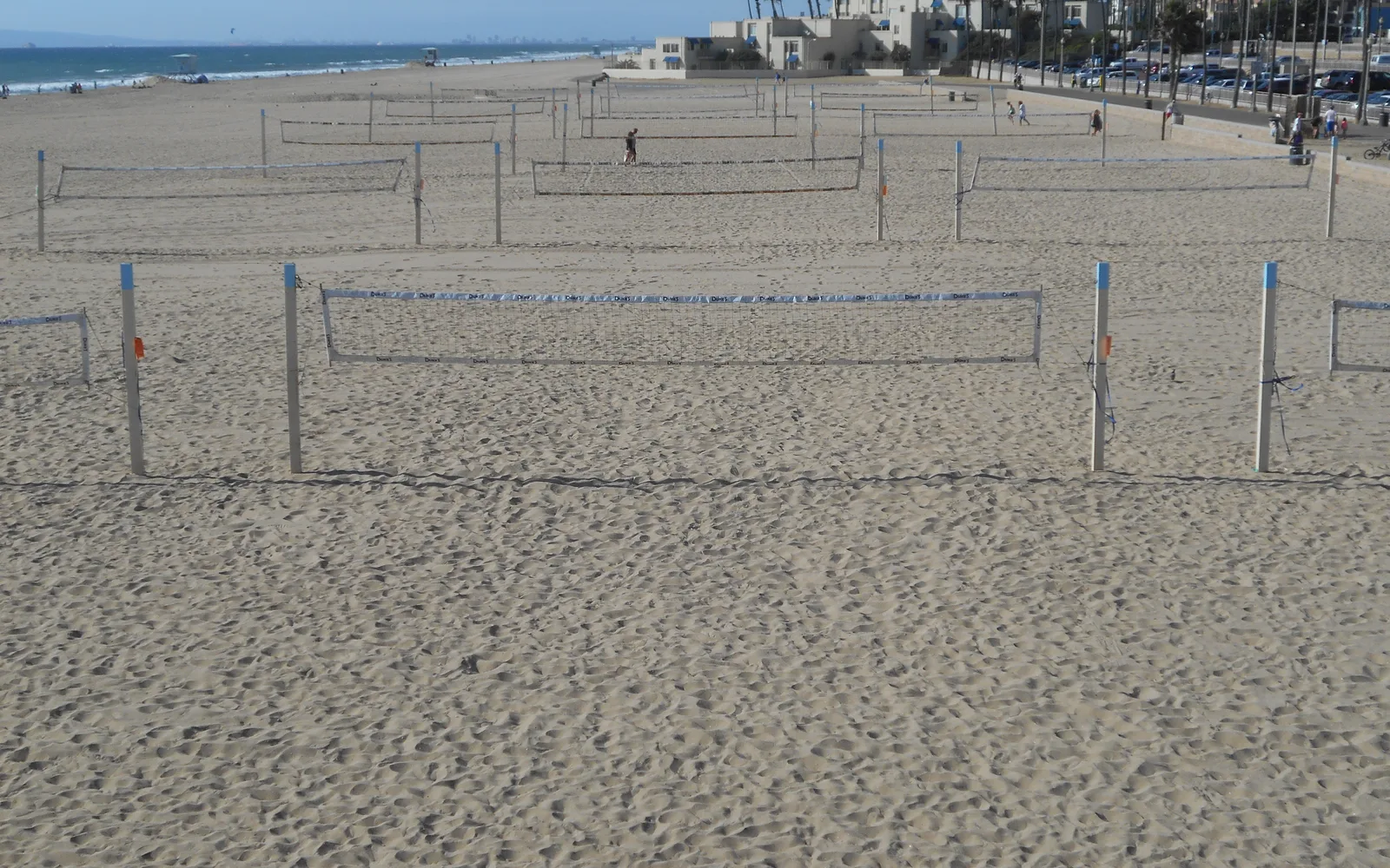 Rows of empty beach volleyball courts beside the ocean in Huntington Beach